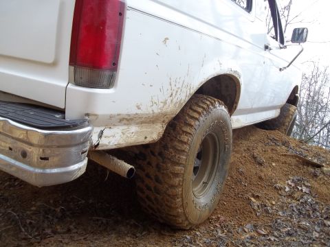 1990 Ford Bronco - This white 1990 Ford Bronco is shown off-road, covered in mud as it navigates a dirt incline.