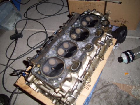 1995 Ford Probe - A disassembled engine cylinder head sits on a cardboard base, with various wires and a bottle nearby.