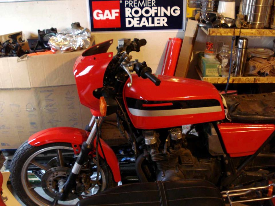 red motorcycle with black seat and fairing, parked indoors near boxes and shelves