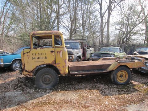 1991 Ford LTD Crown Victoria - A weathered yellow US Navy truck sits in a junkyard with other vehicles.