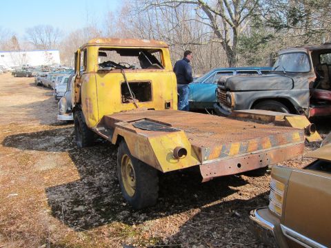 1991 Ford LTD Crown Victoria - A rusty yellow tow truck with a flatbed sits in a yard with other vehicles. A man stands near a blue car.