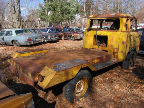 1991 Ford LTD Crown Victoria - Abandoned yellow military truck in a junkyard with other vehicles.