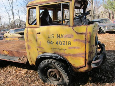 1991 Ford LTD Crown Victoria - A heavily rusted yellow U.S. Navy truck sits in a junkyard with other vehicles.