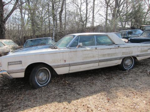 1991 Ford LTD Crown Victoria - A weathered white sedan sits in a junkyard with other vehicles.