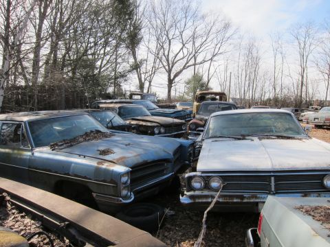 1991 Ford LTD Crown Victoria - A collection of weathered vehicles sits in an outdoor storage lot under a cloudy sky.