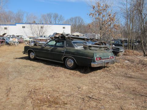 1991 Ford LTD Crown Victoria - This dark green sedan, likely a 1975 model, is seen from the rear with various parts piled on its roof.