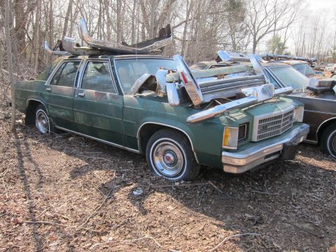 1991 Ford LTD Crown Victoria - Junkyard sedan, possibly a 1980s Ford, loaded with spare chrome bumpers.