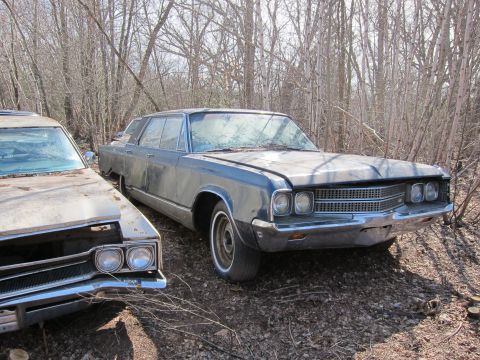1991 Ford LTD Crown Victoria - Two old cars sit abandoned in a wooded area, surrounded by trees and debris.