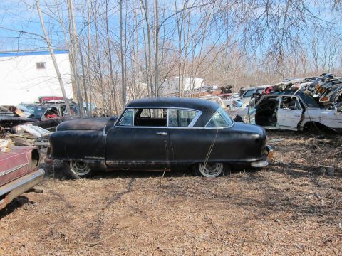 1991 Ford LTD Crown Victoria - A black sedan sits in a junkyard with other vehicles and parts visible in the background.
