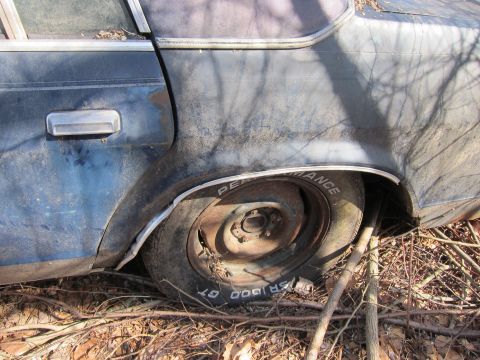 1991 Ford LTD Crown Victoria - Rear wheel and fender of a weathered dark blue sedan, with visible tire text.