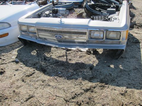1991 Ford LTD Crown Victoria - The front grille and headlights of a Ford Crown Victoria are visible in this junkyard scene.
