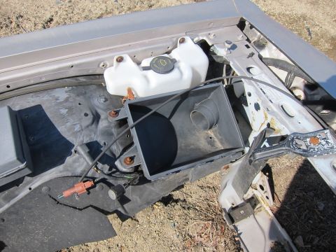 1991 Ford LTD Crown Victoria - Close-up of an engine bay showing an air intake housing and coolant reservoir, with visible rust and damage.