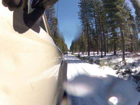 1989 Ford Bronco - A tan SUV travels down a snow-covered forest road, with another vehicle visible in the distance.