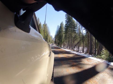 1989 Ford Bronco - A white SUV travels down a tree-lined road with patches of snow on the shoulder.