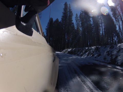 1989 Ford Bronco - Driving on a snowy road through a forest with the sun shining.
