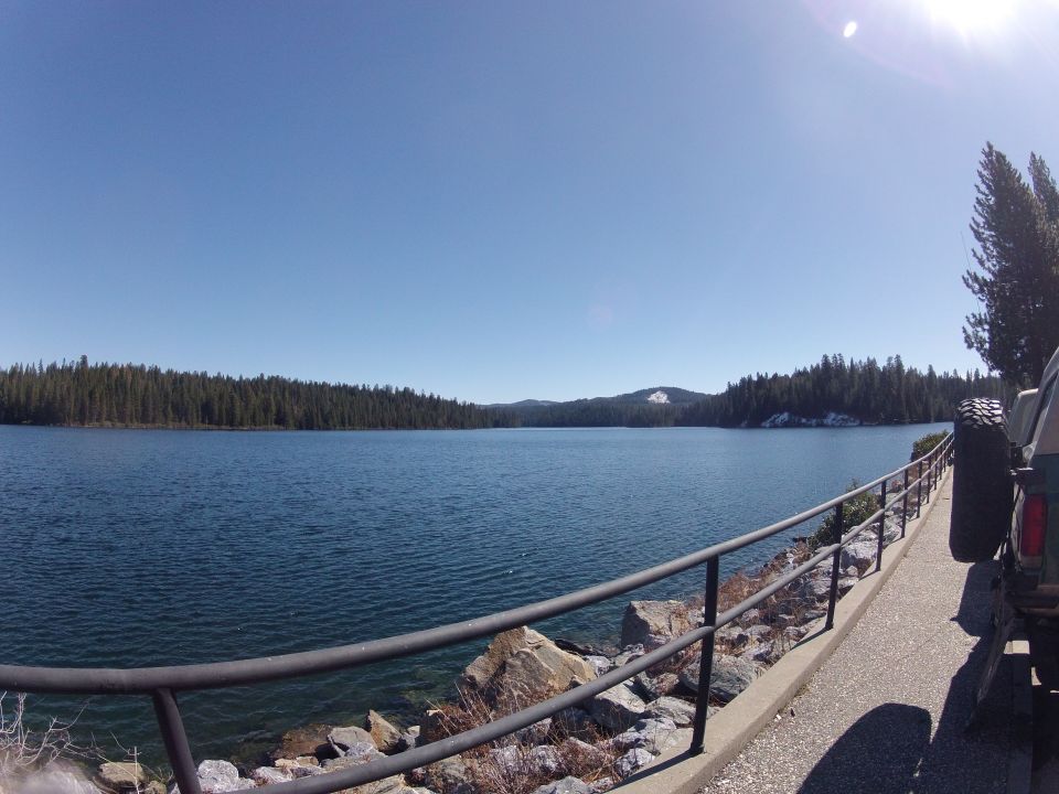 Off-road vehicle with spare tire mounted on back parked next to a railing overlooking a large lake with a tree-lined shore