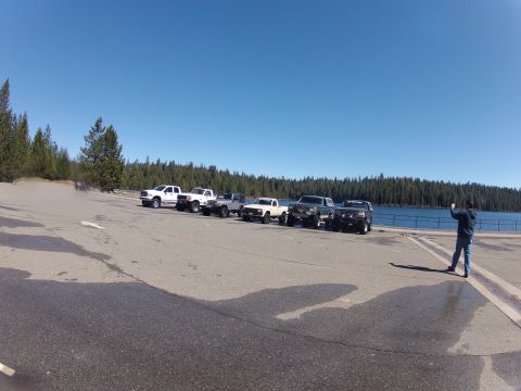 1989 Ford Bronco - Several trucks and SUVs are parked in a line by a lake on a sunny day.