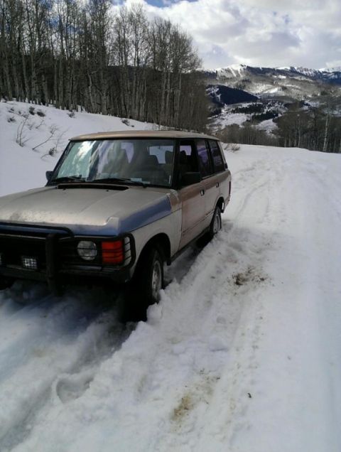 1991 Land Rover Range Rover - A 1991 Land Rover Range Rover navigates a snow-covered mountain path, with trees and snow-capped peaks in the background.