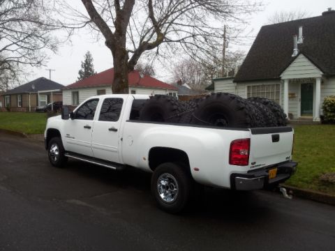 2008 GMC Sierra 3500 - White GMC Sierra 3500 pickup truck with large tires loaded in the bed.