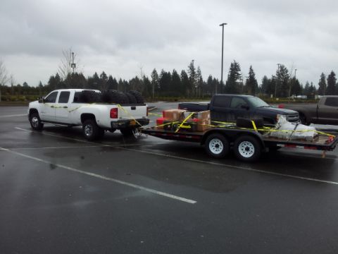 2008 GMC Sierra 3500 - Two pickup trucks are parked in a lot, one towing the other on a trailer.