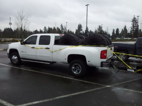 2008 GMC Sierra 3500 - A white dually pickup truck is parked in a lot, carrying several large tires in its bed.