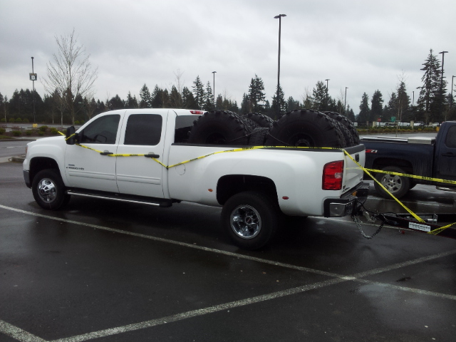 White dually pickup truck loaded with large tires, parked next to another truck