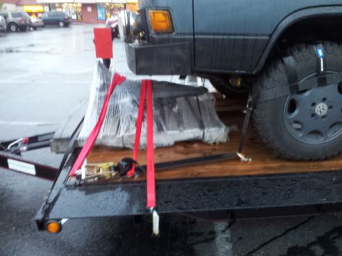 2008 GMC Sierra 3500 - A vehicle engine is secured with red straps to a trailer, ready for transport.
