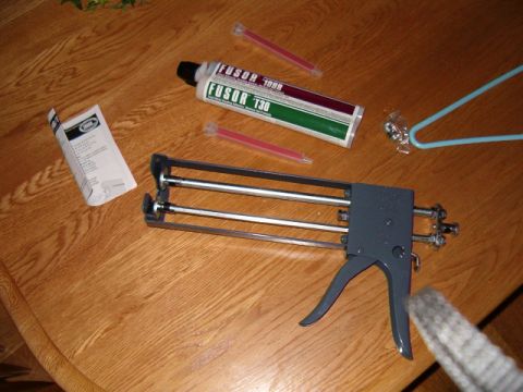 1990 Ford Bronco - A caulking gun, adhesive, and mixing tips are laid out on a wooden surface, suggesting preparation for body work.