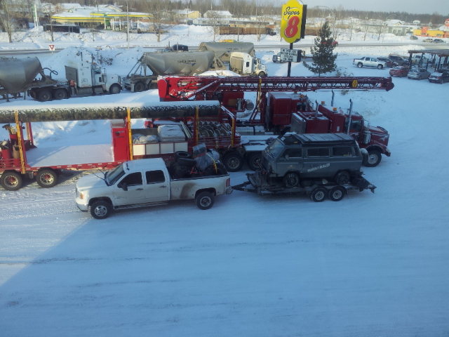 White GMC Sierra pickup truck towing a trailer with a gray van on it, parked in snow