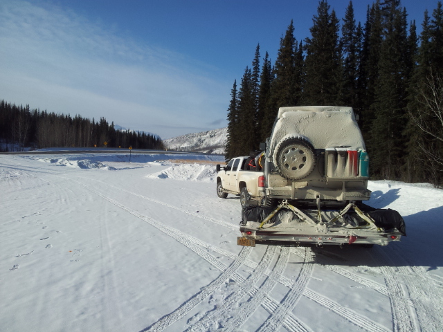 White pickup truck towing a white camper trailer on a snowy road