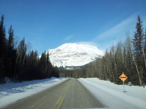 2008 GMC Sierra 3500 - A bumpy road sign warns drivers on a snow-covered highway leading towards a large, snow-capped mountain.