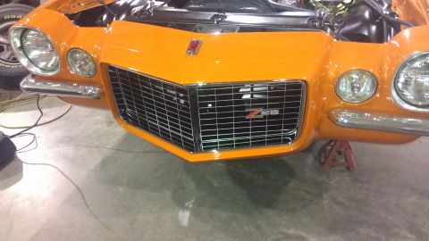1973 Chevrolet Camaro - The front end of an orange Z28 muscle car is shown with its hood open and resting on jack stands.