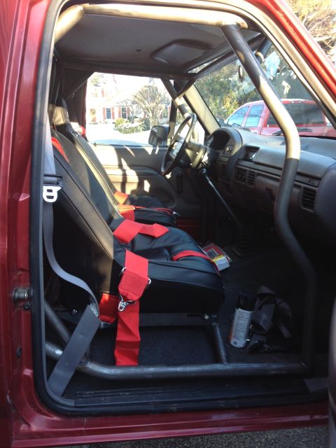 1996 Ford F-150 - The interior of a red 1996 Ford F-150 shows a custom roll cage and racing seats with red harnesses.