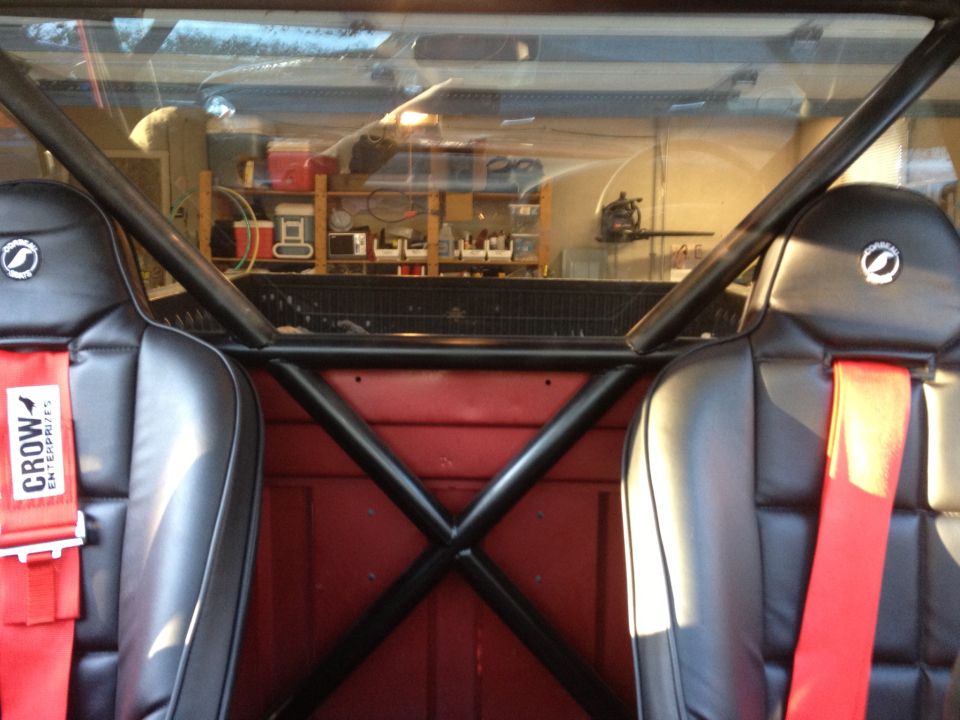 Interior view of racing seats and roll cage in a truck cab. Red racing harnesses visible