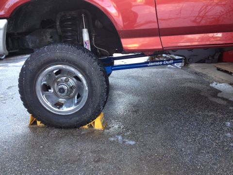 1996 Ford F-150 - Close-up of a red truck's lifted suspension and large tire, with "James Duff" branding on a blue component.