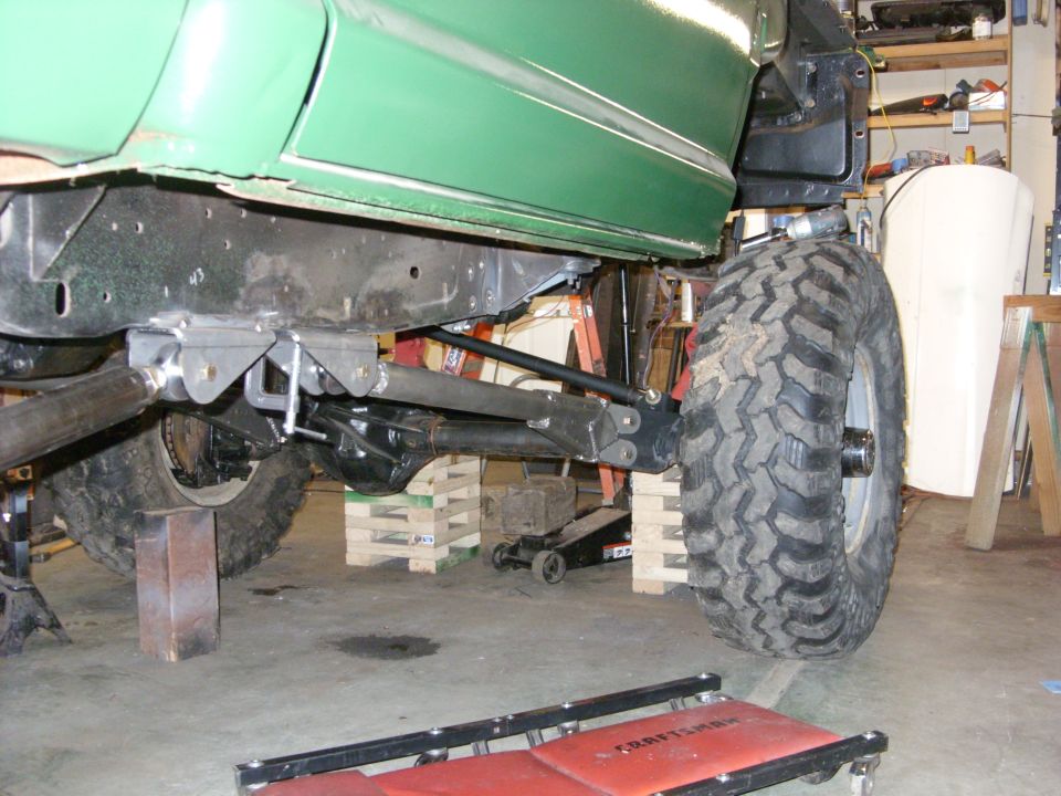 Green truck body above a black frame with large off-road tires and suspension components