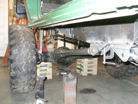 1967 Ford F-250 - Close-up view of the undercarriage and suspension system of a green truck, possibly undergoing modifications.