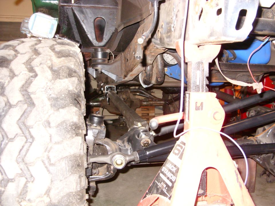 Close-up of a truck's front suspension and chassis, with a large tire on the left and a jack stand on the right