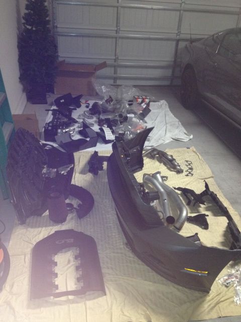 2013 Ford Mustang - Disassembled car parts are laid out on a tarp in front of a dark gray car in a garage.