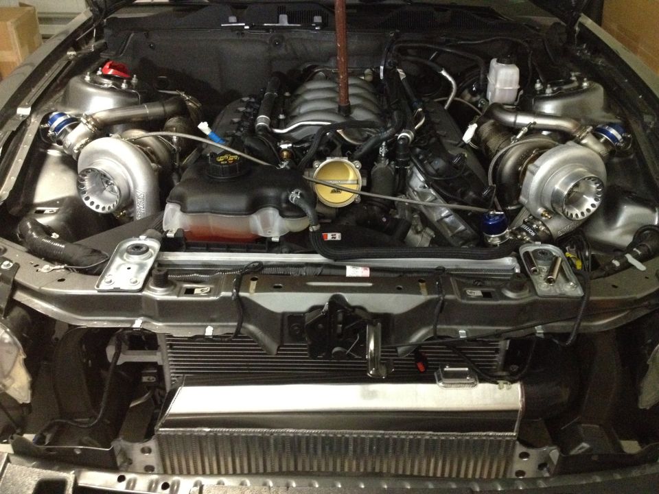 Engine bay with twin turbos, intercooler, and V8 engine components visible. Supermotors.net logo in lower right