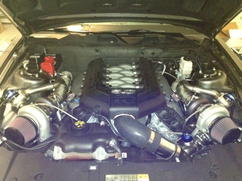 2013 Ford Mustang - The engine bay of a car, modified with twin turbochargers and custom piping, is shown with the hood open.