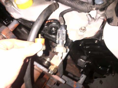 1994 Ford Bronco - Close-up of an engine component with a hand holding a sensor, showing electrical connections.