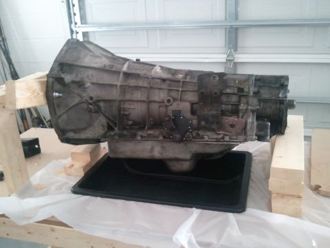 1994 Ford Bronco - A transmission part is shown resting on wooden supports over a black drip pan.