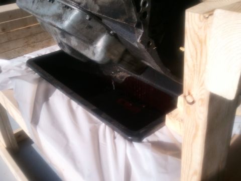 1994 Ford Bronco - Transmission pan draining fluid into a catch pan, supported by wooden bracing.