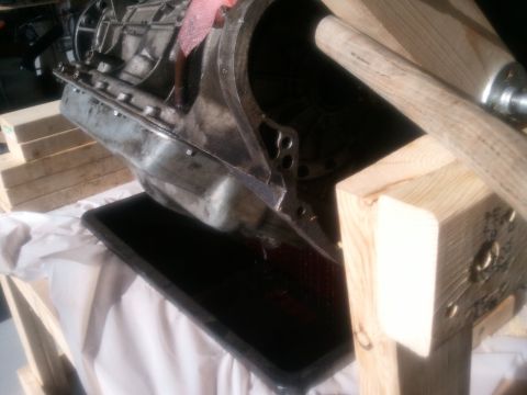1994 Ford Bronco - A transmission assembly is shown draining fluid into a black pan, resting on wooden supports.