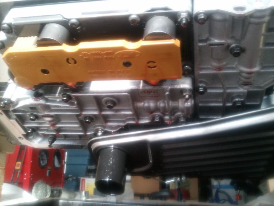 Yellow Ford-stamped transmission part attached to a silver transmission casing