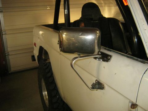 1970 Ford Bronco - A white 1970 Ford Bronco is viewed from the front 3/4 angle, showing its chrome side mirror and black interior.