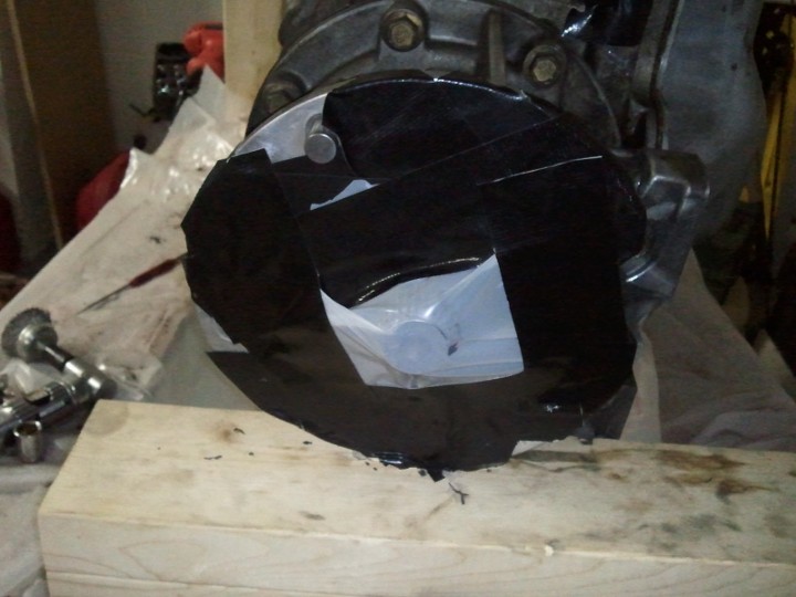 Transmission housing covered in black tape, sitting on a wooden block. Some tools are visible to the left