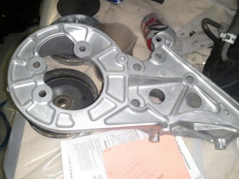 1994 Ford Bronco - Aluminum bracket with pulleys and hoses, possibly for a vehicle engine, with a can and manual nearby.