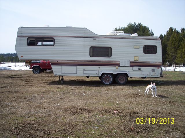 White fifth wheel trailer parked next to a red pickup truck in a grassy field with a dog